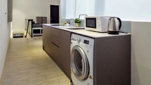 A modern kitchen with a built-in washer, a microwave, and a kettle on the counter. - Hutton Suites Hotel Managed By The Ascott Limited (George Town)