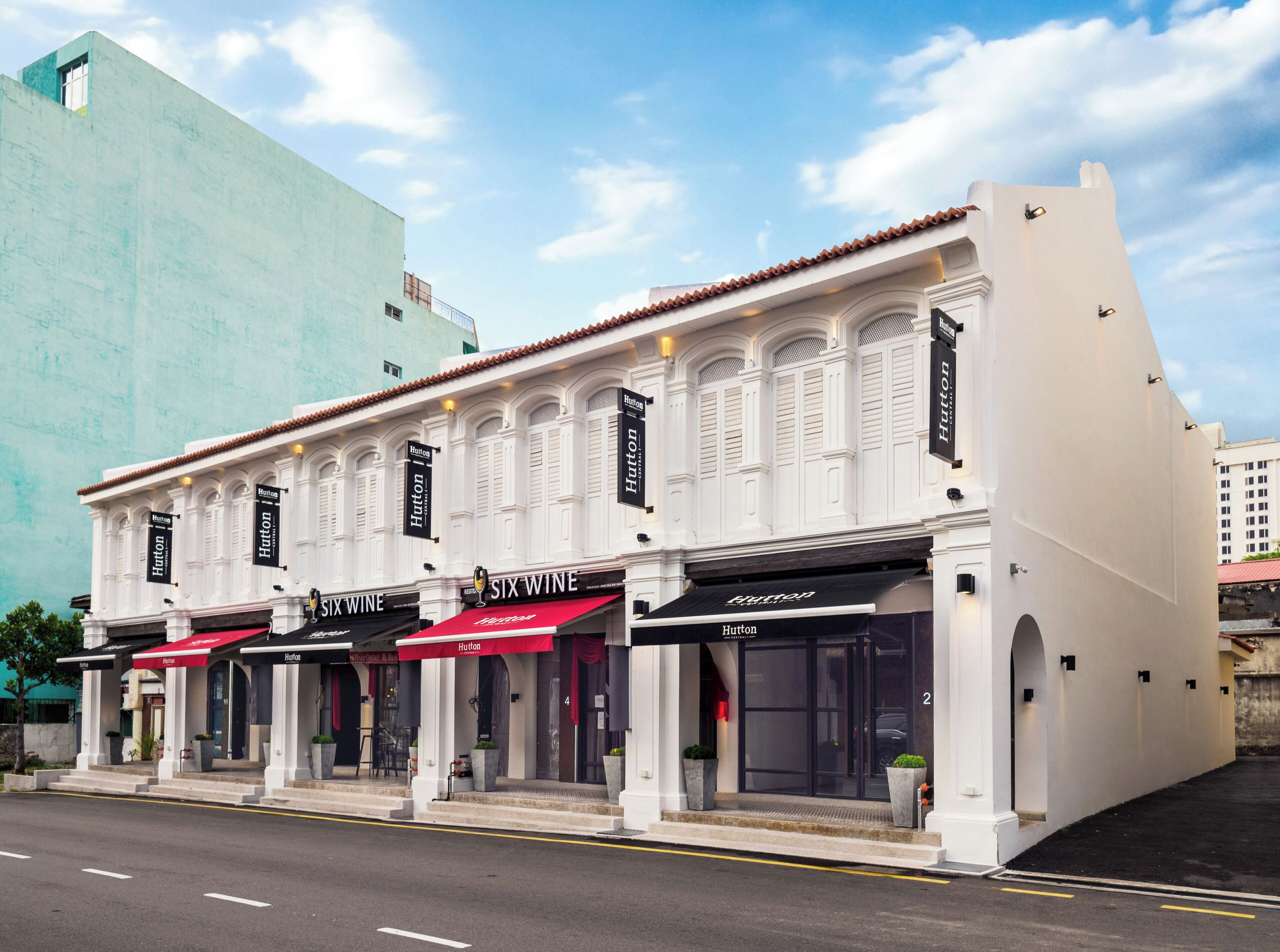 A row of white buildings with storefronts, including a Six Wine bar, under a clear sky.