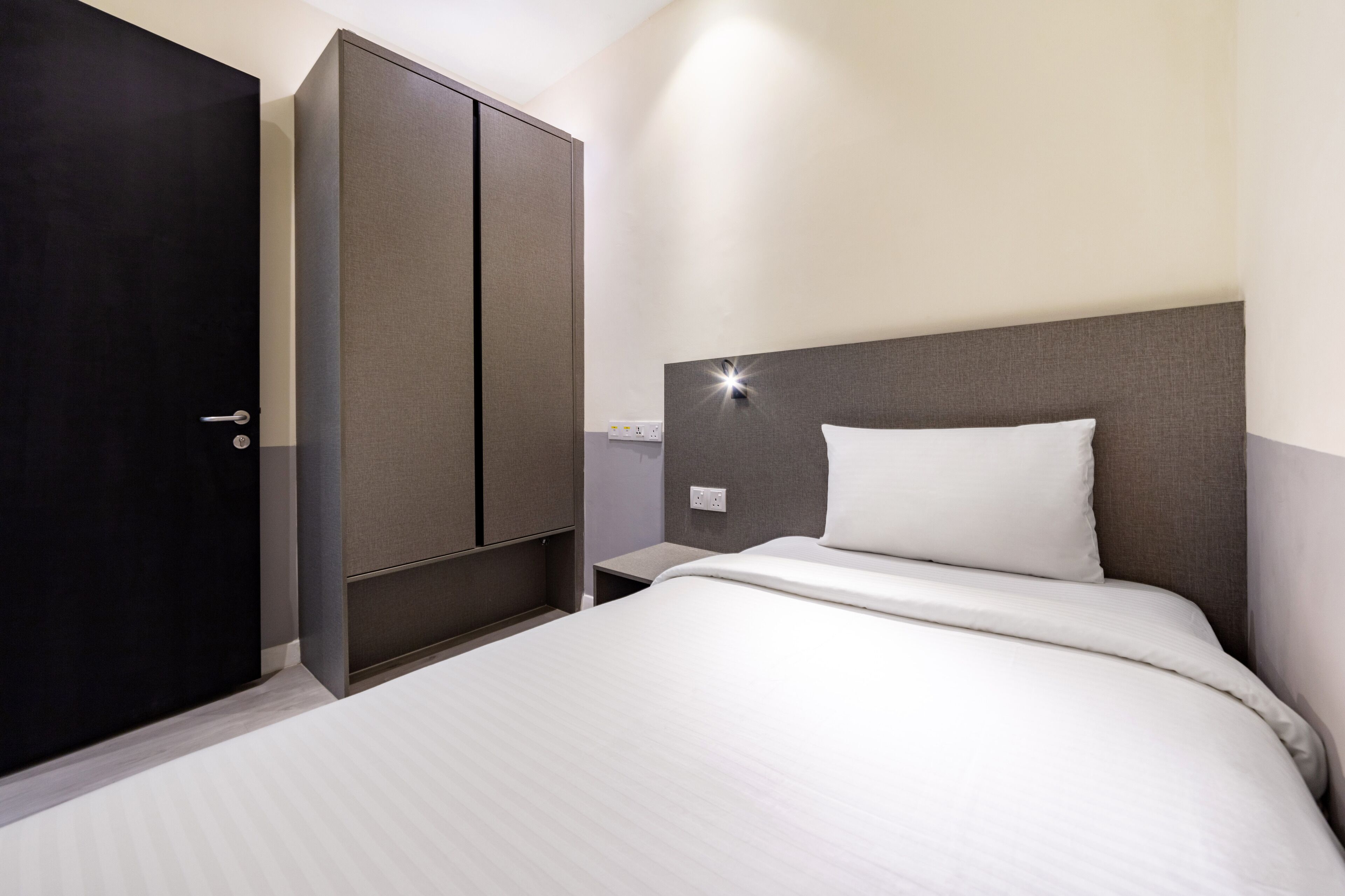 A hotel room with a bed, a wardrobe, a nightstand, and a wall-mounted light.