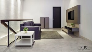 A modern living room with a sofa, a coffee table, a TV mounted on the wall, and a staircase with a railing. - Hutton Suites Hotel Managed By The Ascott Limited (George Town)
