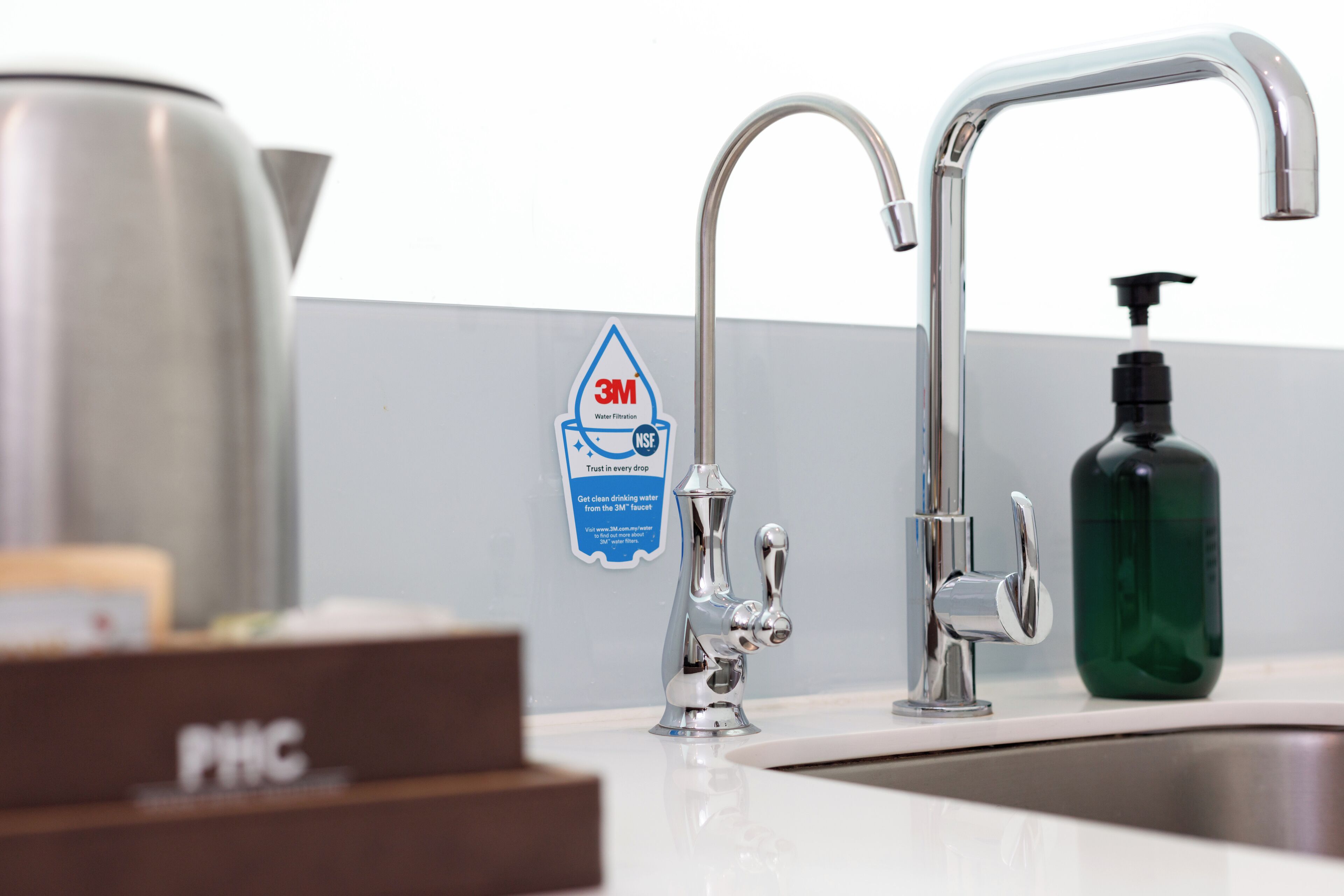 A modern bathroom with a stainless steel sink, a 3M water filtration sign, and a PHC box.