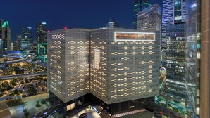 Un edificio moderno con un diseño angular distintivo, que incluye una terraza en la azotea y un aparcamiento con varios coches.