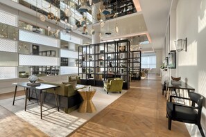 Un interior amplio con techo alto, una zona de estar central con una mesa de centro y una gran estantería llena de objetos variados.