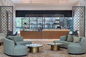 A modern lounge area with two sofas, a coffee table, and a bar area with shelves of bottles and glasses. - Atheel KAFD Hotel (Riyadh)