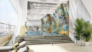 Zona de piscina interior moderna con vistas a la ciudad, una escalera que conduce a un nivel superior y un muro decorado.