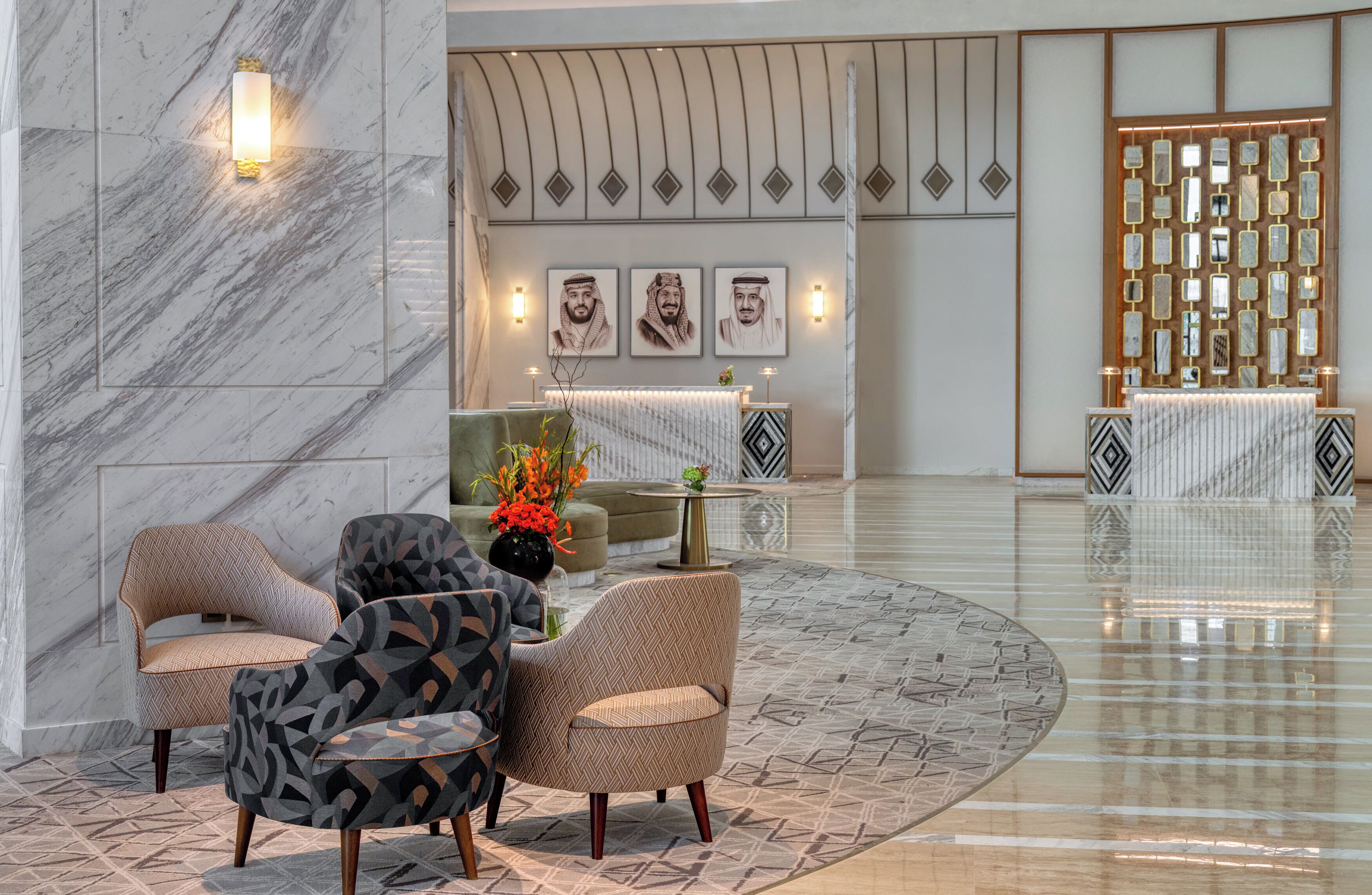 Un vestíbulo con paredes de mármol, una mesa de recepción y una zona de estar con sillones estampados.