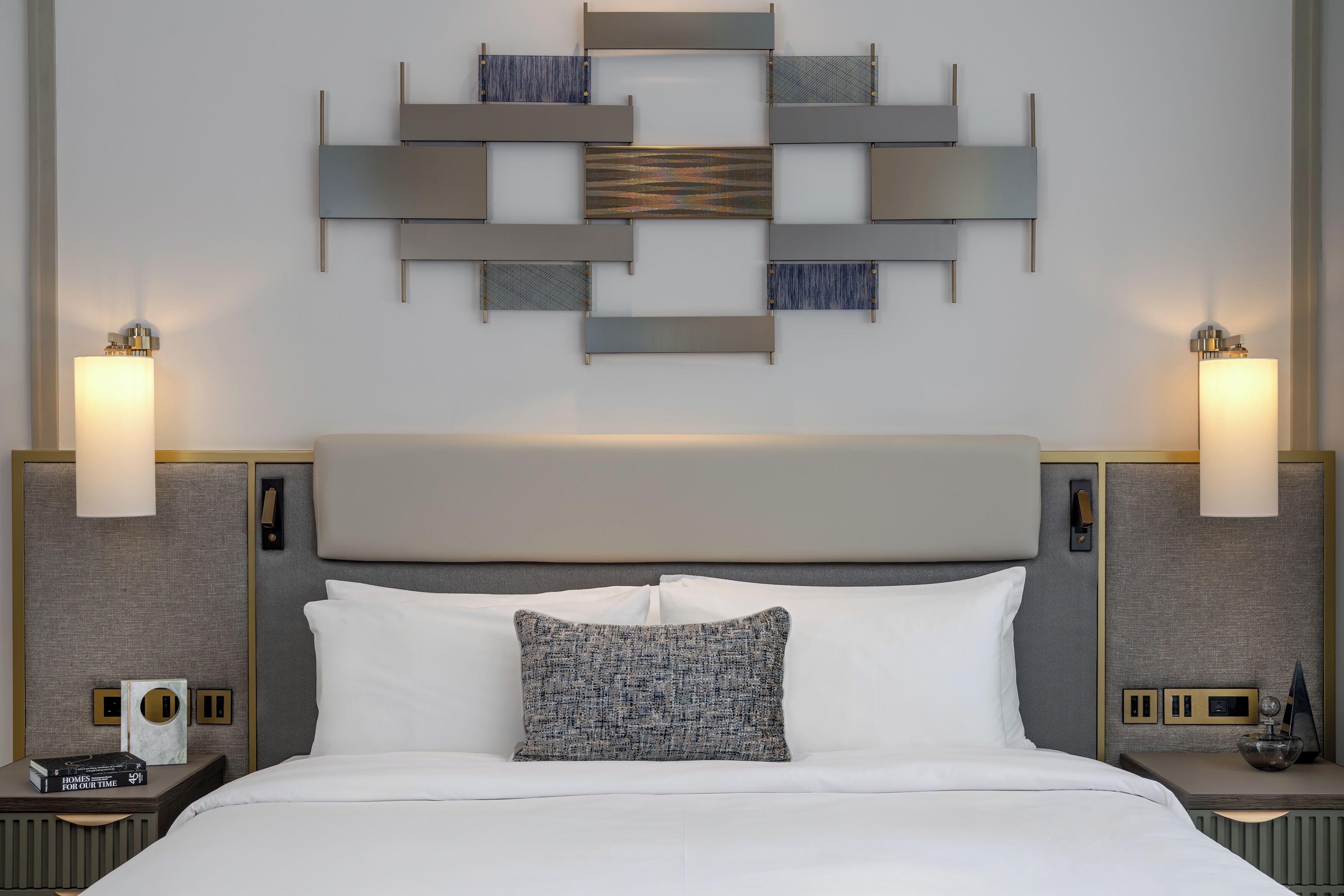 A hotel room with a large bed, two bedside tables, a wall-mounted light fixture, and a decorative wall panel.