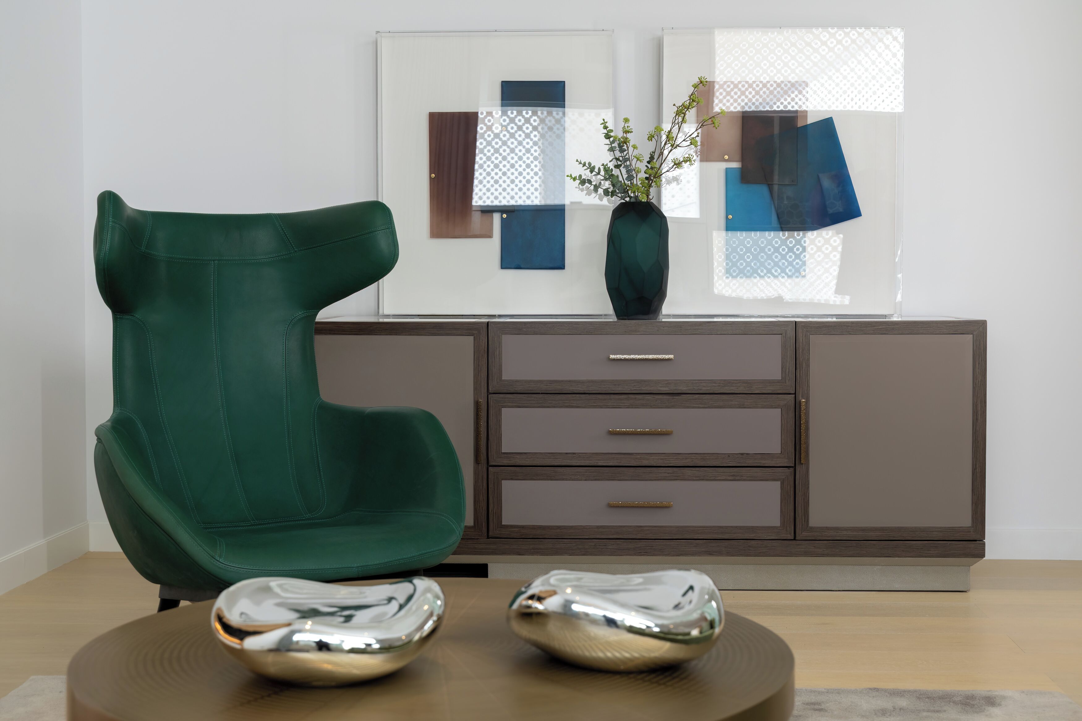 A green chair, a cabinet with drawers, and a vase with a plant on a table.