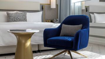 A hotel room with a bed, a blue armchair, a small round table, and a patterned pillow.