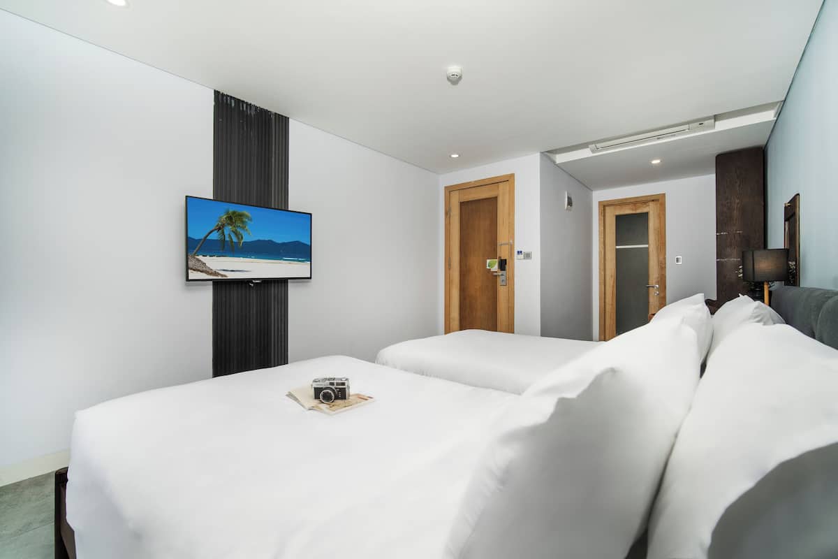 Hotellihuone, jossa on kaksi sänkyä, seinälle asennettu televisio ja ovi, joka johtaa toiseen huoneeseen.