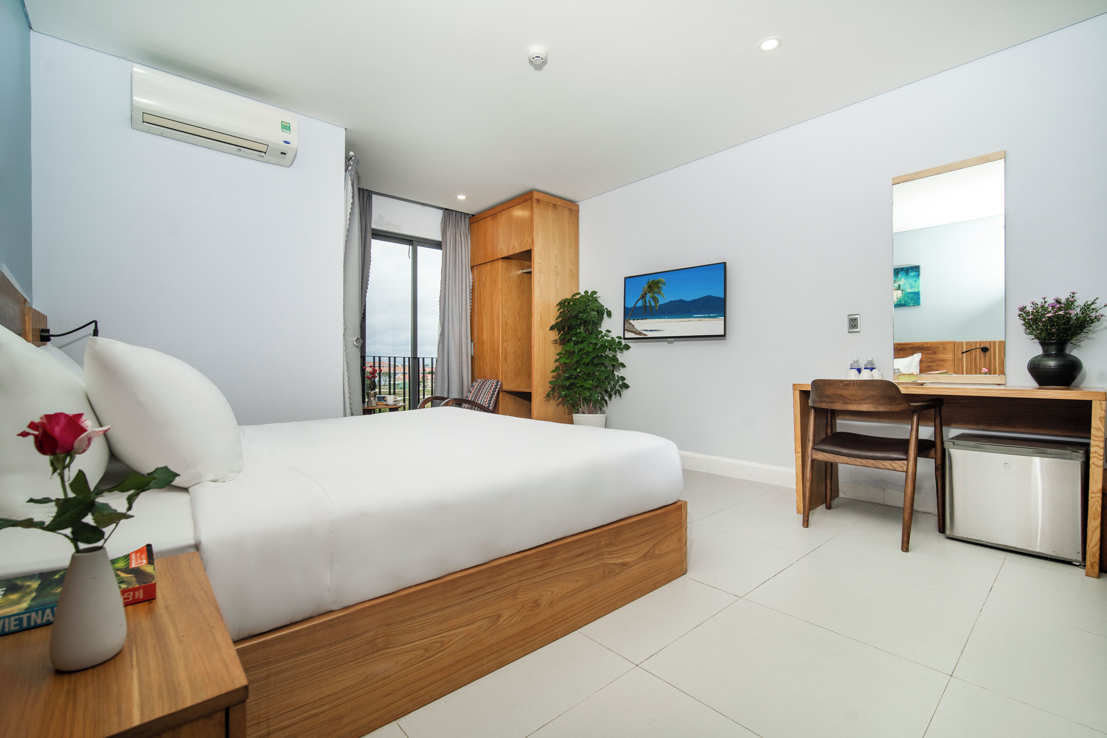 A modern hotel room with a bed, desk, and a small refrigerator.