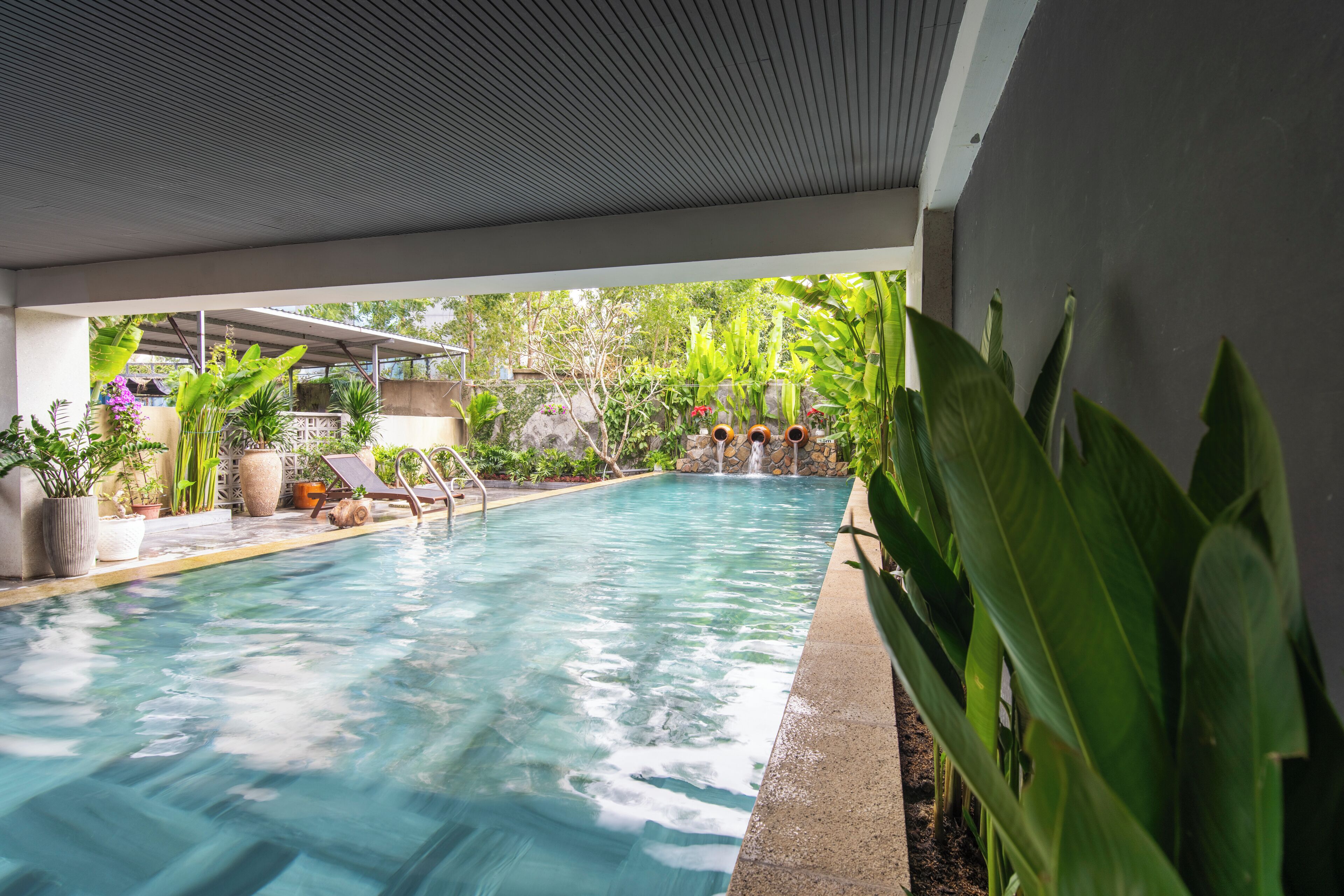 A swimming pool with clear water, surrounded by potted plants and a lounge area.