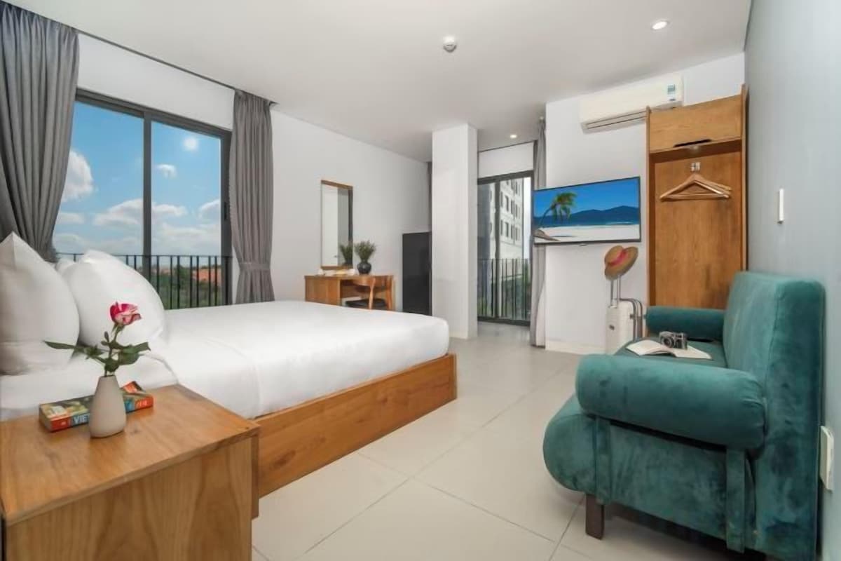 Una habitación de hotel moderna con una cama grande, un escritorio, un sillón verde y vistas al exterior.