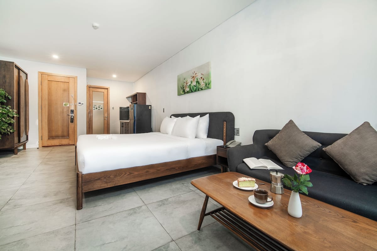 Moderni hotellihuone, jossa on puinen sänky, musta sohva, kahvipöytä, jonka päällä on kakku, maljakko kukkineen ja seinällä taulu.