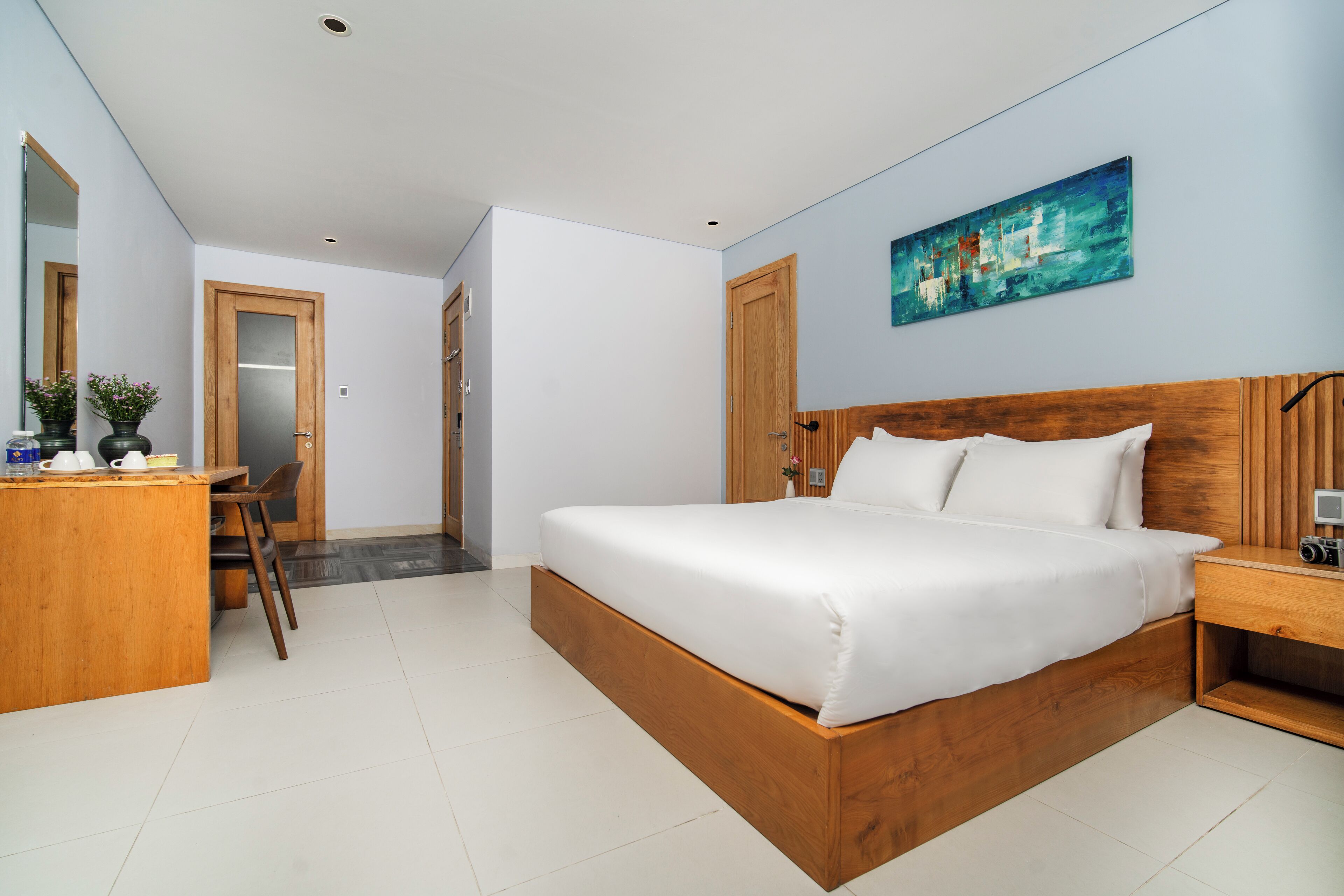 A modern bedroom with a wooden bed, a desk with a chair, and a painting on the wall.