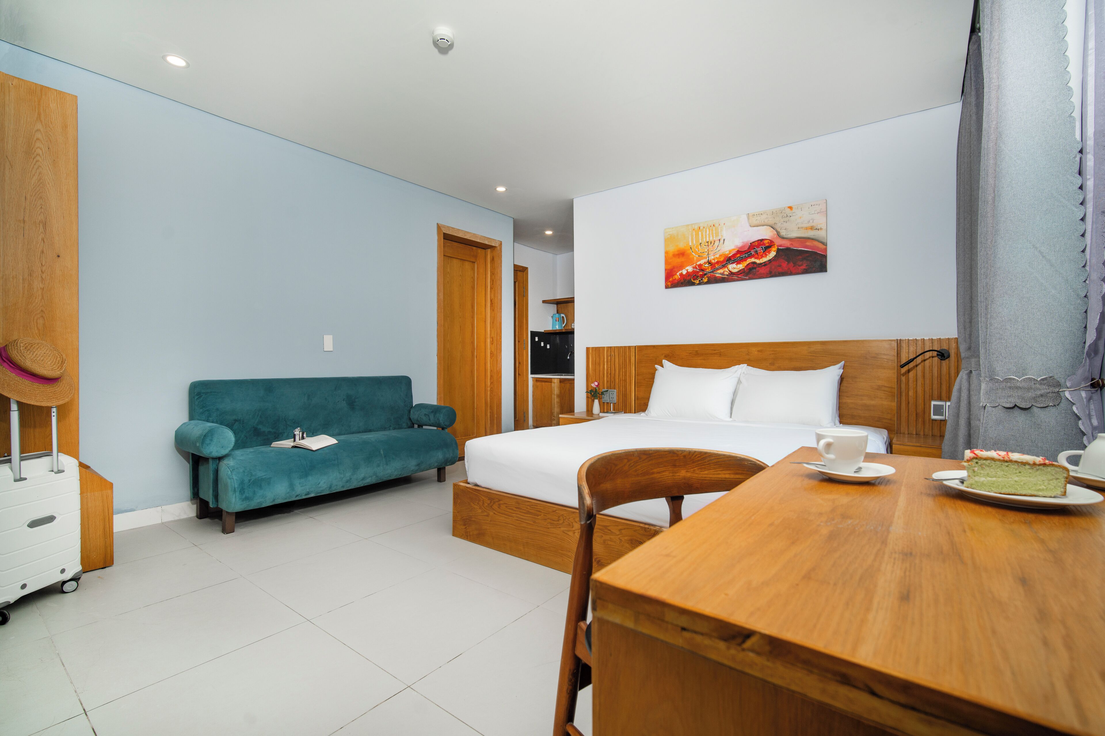 A hotel room with a bed, a wooden table with a cake, a teal sofa, and a wooden wardrobe.
