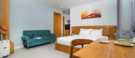 A hotel room with a bed, a wooden table with a cake, a teal sofa, and a wooden wardrobe.