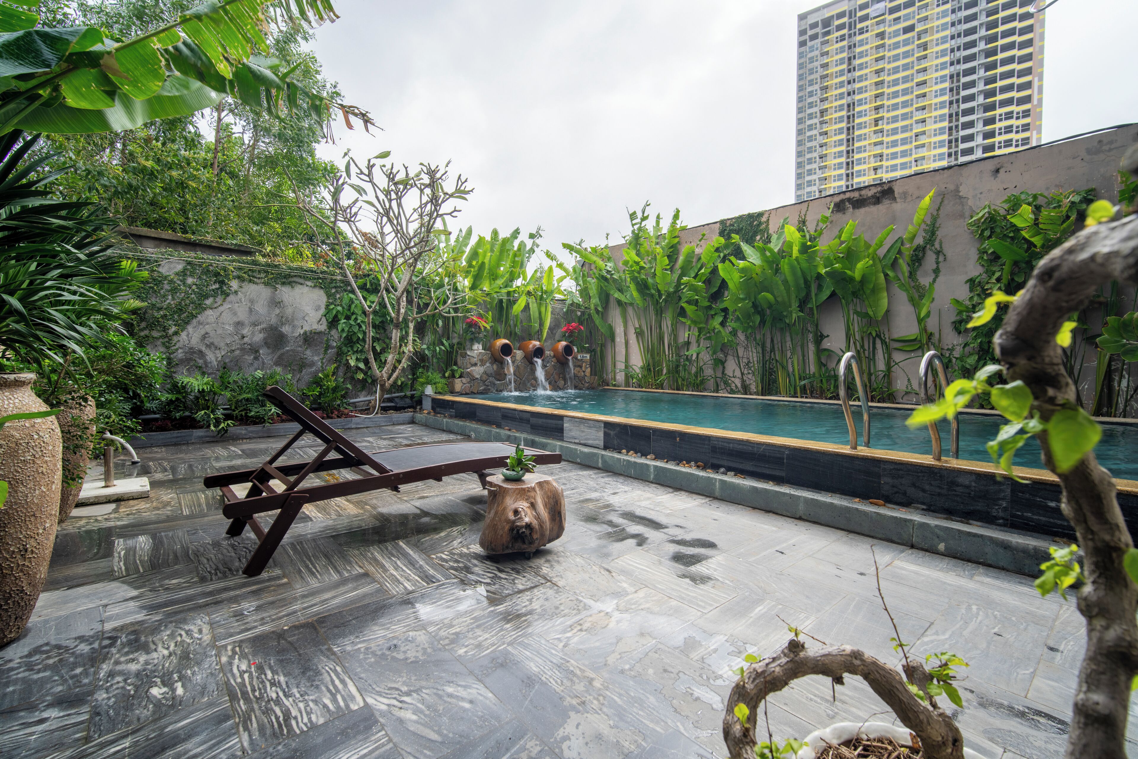 Un jardín en la azotea con piscina, suelo de piedra y una tumbona de madera.