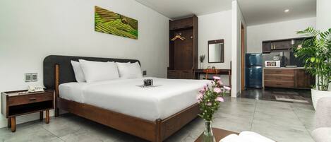 A modern hotel room with a large bed, bedside table, and a small desk with a chair.