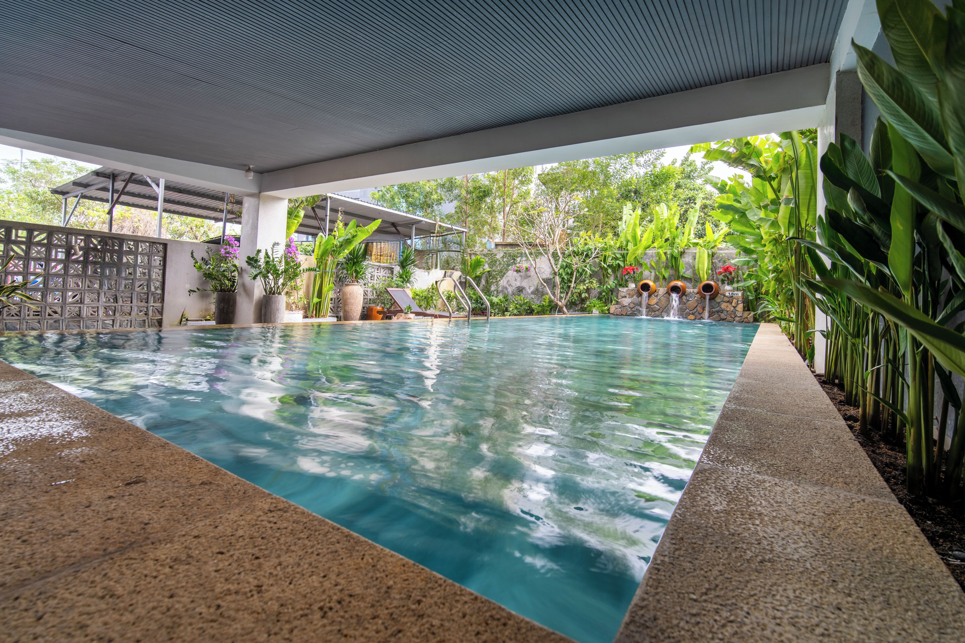Une piscine à l’eau d’un bleu limpide, entourée de plantes en pot et dotée d’un espace abrité sous un toit.