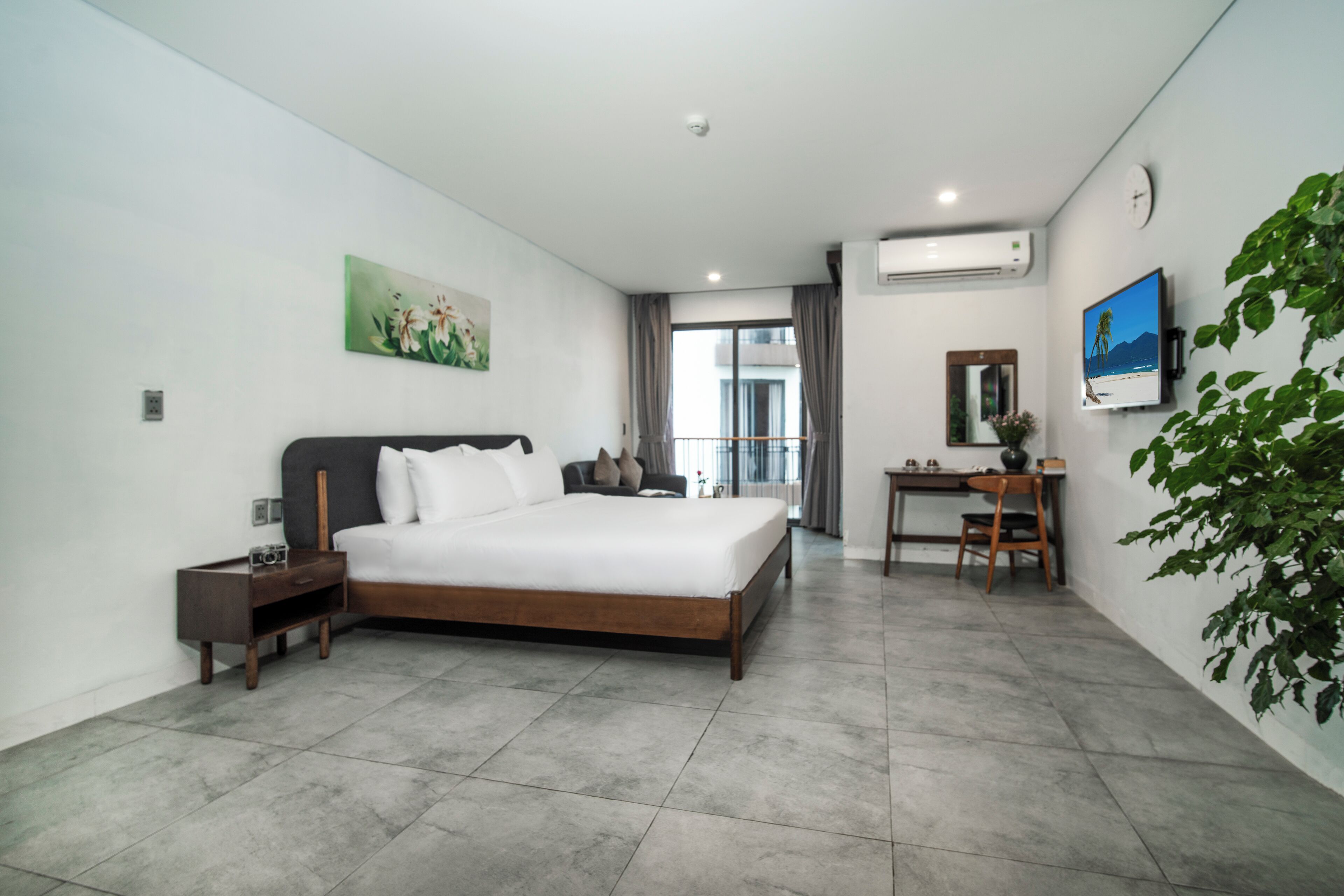 A modern hotel room with a large bed, a desk, a chair, and a potted plant.