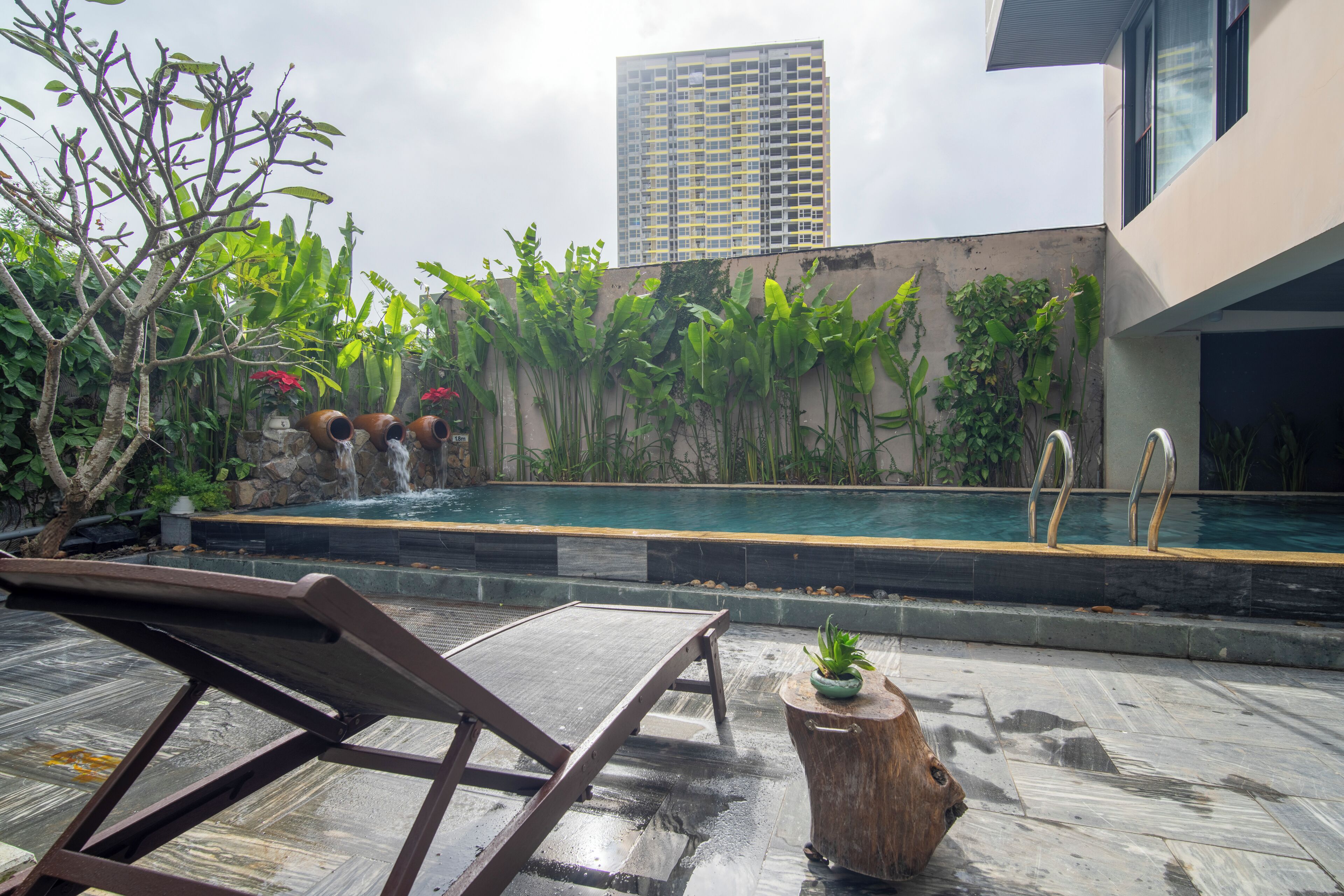 A rooftop pool area with a lounge chair, a small waterfall, and lush greenery.