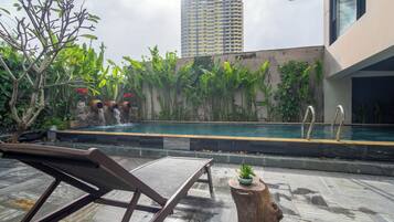 A rooftop pool area with a lounge chair, a small waterfall, and lush greenery.