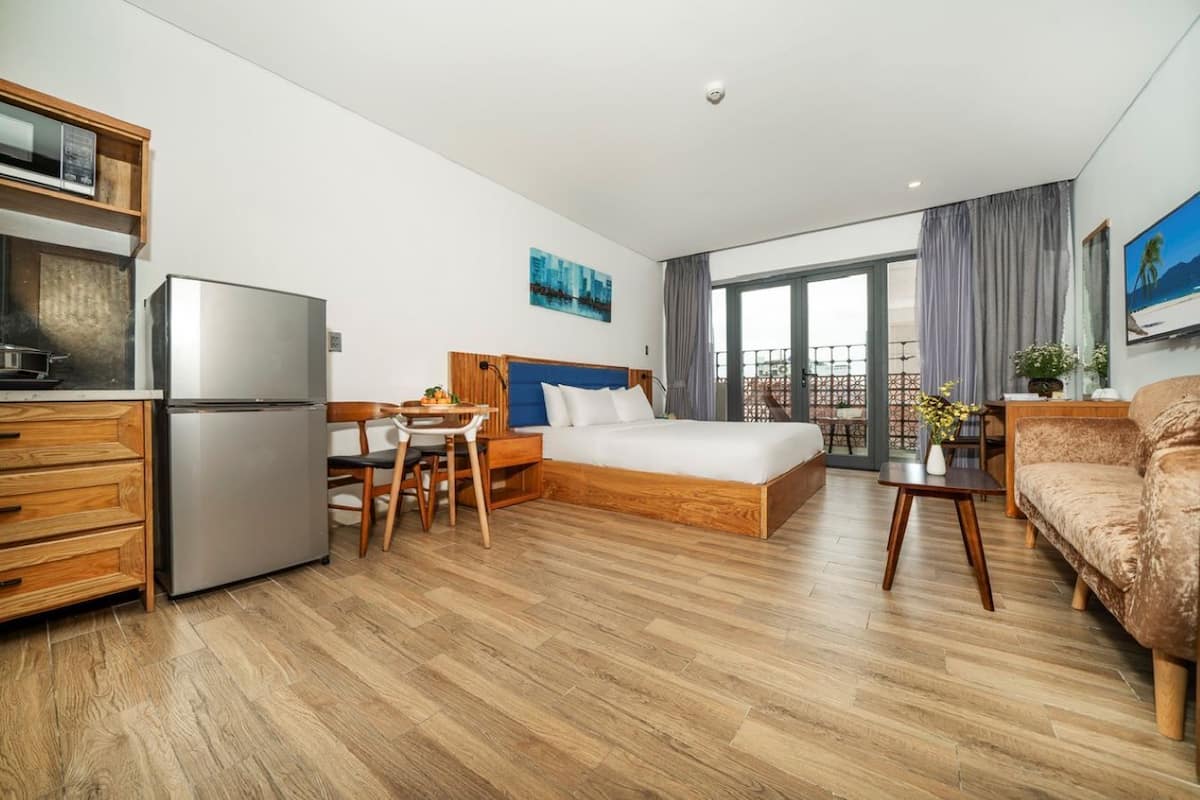 Hotellihuone, jossa on sänky, työpöytä, pieni keittiönurkkaus ja parveke, jolta on näkymä.
