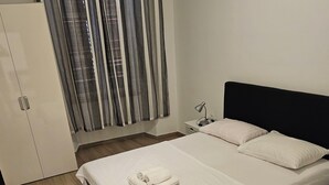 A neatly made bed with white linens and a folded towel, a bedside table with a lamp, and a wardrobe with a sliding door. - Apartment Jadran (Zadar)
