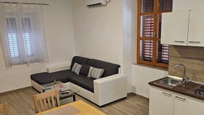 A compact living space with a sofa, a dining table, and a kitchen area including a sink and cabinets. - Apartment Jadran (Zadar)