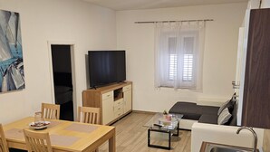A compact living space with a dining area, a sofa, a TV, a window with curtains, and a kitchenette. - Apartment Jadran (Zadar)