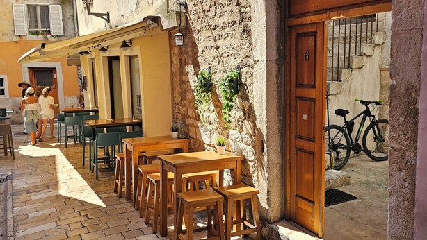 A narrow street with outdoor seating and a bicycle parked by the entrance. - Apartment Jadran (Zadar)