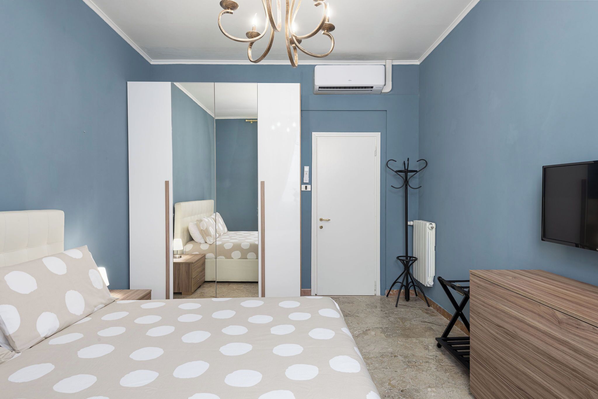 Quarto com cama, guarda-roupa, espelho, radiador e televisão.
