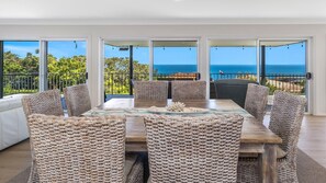 Enjoy meals with a view of the ocean from this dining area featuring a wooden table and woven chairs.