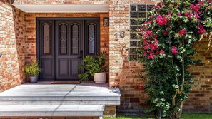 Welcome to a charming home with a brick facade, featuring a wooden deck and a beautiful flowering vine.