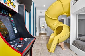 A room with a yellow spiral slide, a gaming console, and a bed. - Family Heated Pool | Kids Room | Mini Golf | Near Bucs (Tampa)