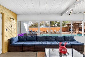 A modern outdoor living area with a large sectional sofa, a glass coffee table, and a view of a backyard swimming pool. - Family Heated Pool | Kids Room | Mini Golf | Near Bucs (Tampa)