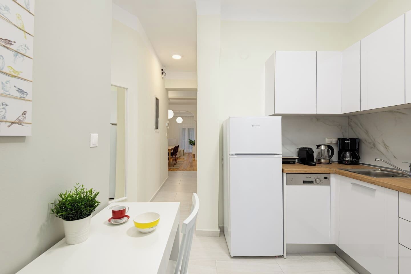 A modern kitchen with white cabinets, a built-in dishwasher, and a coffee maker.