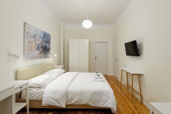 A hotel room with a bed, bedside table, TV, wardrobe, and artwork on the wall.