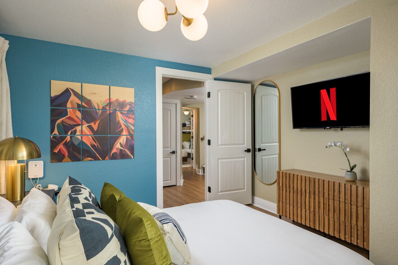 A hotel room with a bed, a wall-mounted TV displaying the Netflix logo, a painting, and a wooden console.