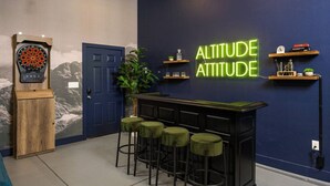 Baaritiski ja -tuoleja, dart-taulu ja neonvalomainos, jossa lukee: ”ALTITUDE ATTITUDE”.