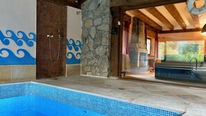 A swimming pool with a tiled edge, a stone wall, and a wooden ceiling. - Luxury villa with heated swimming pool and games room, nestled in the mountains (Navafría)