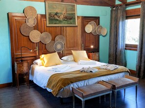 A hotel room with a bed, a bench, a wooden headboard, a painting, and a window with curtains.