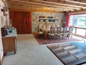 Un comedor con una mesa y sillas de madera, una pared de piedra y vistas a través de una ventana.