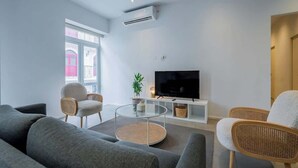 A modern living room with a grey sofa, a round glass coffee table, wicker chairs, a flat-screen TV on a white stand, and a potted plant. - w*| Sublime 2BR w/ Rooftop In Casco Antiguo (Panamá)