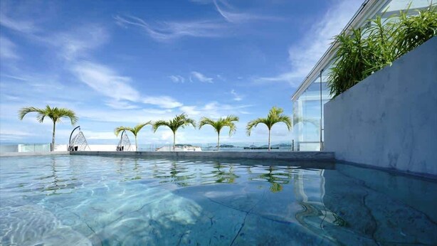 A clear swimming pool with a view of the ocean, surrounded by palm trees and a modern building. - w*| Sublime 2BR w/ Rooftop In Casco Antiguo (Panamá)