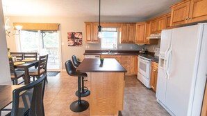 Una cocina moderna con armarios de madera, una isla central, un refrigerador y un comedor con sillas y una mesa.