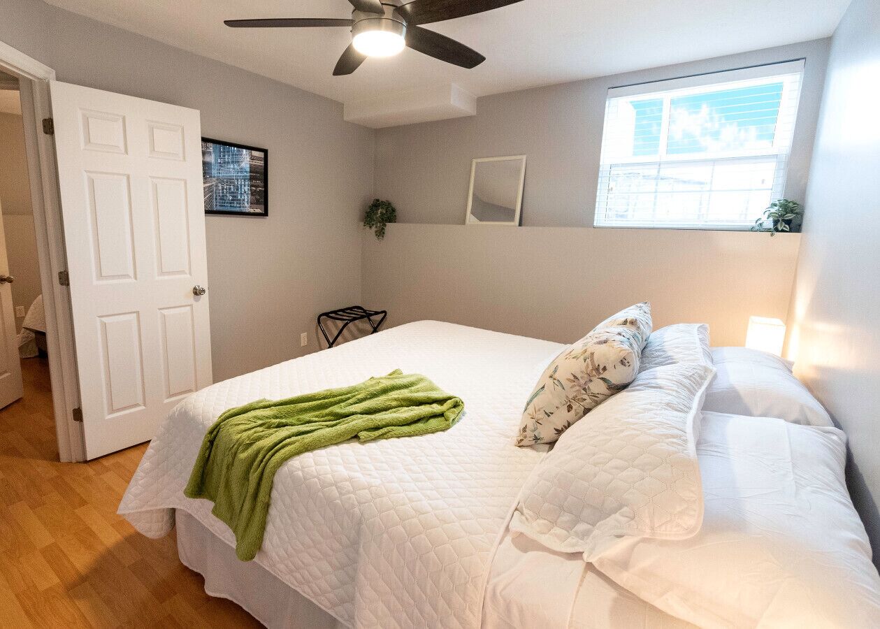 Une chambre à coucher avec un lit, un ventilateur de plafond, une fenêtre et une porte.