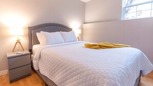 Una cama bien hecha con un edredón blanco acolchado, una lámpara de noche y una mesita de noche con lámpara.