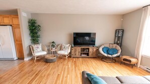 Una sala de estar con piso de madera, un sofá, dos sillones, un televisor y una mesita.